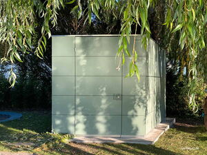 . Ein minimalistisches, modernes Gartenhaus aus grünen Platten, umgeben von Bäumen und Schatten.