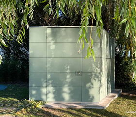 . Ein minimalistisches, modernes Gartenhaus aus grünen Platten, umgeben von Bäumen und Schatten.