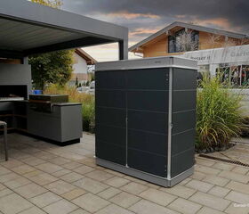 . Moderne Außenküche mit Grill und dunklem Gartenkabinett auf einer Terrasse bei Abenddämmerung.