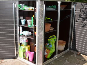 . The image shows a storage cabinet with multiple shelves. Here's a breakdown of the contents:

1. **Top Shelf:**
   - Various small bags, possibly with gardening materials.
   - Some items in containers.

2. **Middle Shelves:**
   - A metal bucket.
   - A green bottle.
   - Various gardening tools and materials, such as seeds and plant pots.

3. **Bottom Shelf:**
   - Cans and small bags.
   - A pink watering can.
   - Larger bags, possibly potting soil or fertilizer.

4. **Right Section:**
   - More bags, potentially soil or compost.
   - Clay pots and trays.

This setup appears to be for gardening supplies and tools.