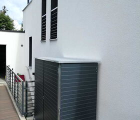 Ein modernes Gebäude mit einem grauen Außenlager neben einer Holzterrasse.