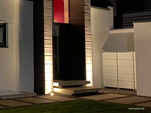 . Ein beleuchteter Hauseingang mit Treppen und moderner Architektur in der Nacht.