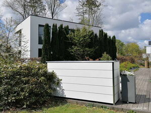 . Modernes Haus mit Garten, Bäumen und weißem Pflanzbehälter im Vordergrund.