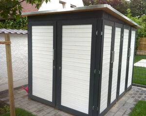 This image depicts a small garden shed or storage building. It has several doors with handles and a flat roof. The exterior is designed with a modern style featuring horizontal siding. The shed is located outdoors, with a paved pathway leading to it and grass surrounding the area.