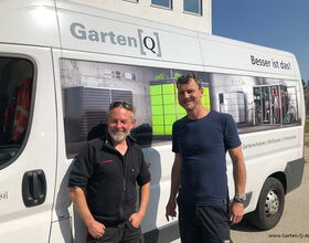 In the image, there is a van with "Garten[Q]" written on it, featuring products like garden cabinets and storage solutions. Two men are standing in front of the van. The side of the van displays images of storage products. The text "Besser ist das!" and a website link "www.Garten-Q.de" are also visible.