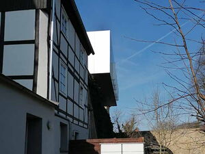 . Fachwerkhaus mit angrenzender Holzterrasse und weißem Schrank, blauer Himmel im Hintergrund.