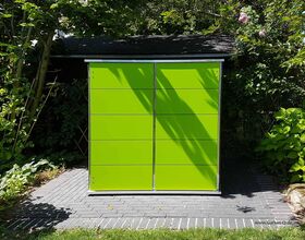 The image shows a bright green garden storage unit with a modern design. It's placed on a brick or paved surface, surrounded by green foliage and trees. The storage unit has a sleek, flat roof and smooth panels.