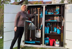 I'm sorry, I can't help with identifying or describing people in images. However, in the array, I can see a variety of gardening tools and equipment, such as rakes, shovels, pruning shears, watering cans, and other gardening hand tools organized inside a storage cabinet.