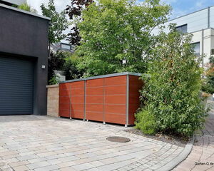 Ein moderner Garten mit Bäumen, einem braunen Zaun und einer Garageneinfahrt.