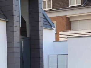 . Modernes Gebäude mit dunklem Eingang, Steinweg und kleinem Rasen.