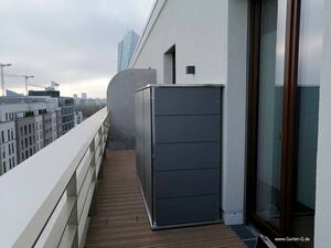 . Ein Balkon mit einem grauen Schrank im Vordergrund und Stadtansicht im Hintergrund.