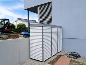 . Ein weißer Gartenschrank an einer blauen Wand, daneben Bauarbeiten mit Bagger.