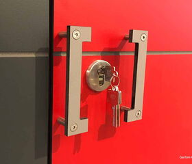 . Roter Schrank mit silbernem Türgriff und Schloss, darin stecken zwei Schlüssel.