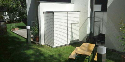 Moderner Garten mit Holzbank, Tisch und weißen Schuppen an der Hauswand.
