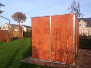 . Ein Garten mit Rasen, Bäumen und einer kleinen modernen Holzhütte.