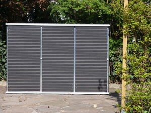 . The image appears to show an outdoor solar panel installed in a garden or backyard setting. It is standing vertically on a paved area with plants and trees surrounding it.