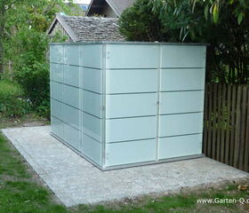. The image shows a modern, cube-shaped garden shed or storage unit with a sleek design. The walls appear to be made of frosted glass or a similar material with horizontal lines. It's set on a paved area in a garden, surrounded by grass, trees, and a wooden fence.