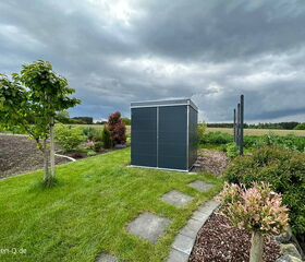 . Ein moderner Gartenschuppen auf einem gepflegten Rasen mit Bäumen und Büschen unter bewölktem Himmel.
