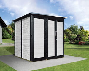 The image shows a modern garden shed with a flat roof and light-colored walls framed in dark trim. It's situated on a concrete pad in a green, landscaped yard with grass and shrubs. In the background, there is a house and some trees under a partly cloudy sky.