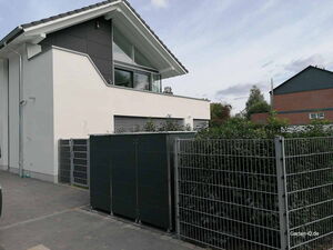 . Modernes Haus mit Gartenzaun und Hecken, klare Linien und dunkle Akzente in der Gestaltung.