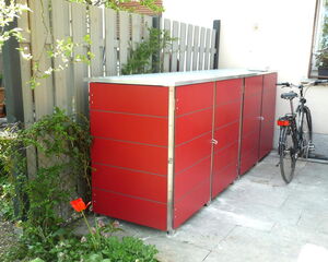 . The image shows a row of red storage cabinets outdoors, placed beside a wooden fence. There's foliage and flowers nearby, along with a bicycle parked adjacent to the cabinets.