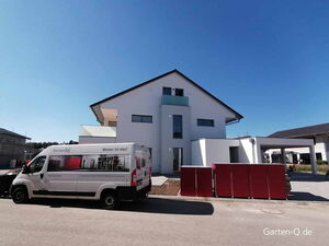 Ein modernes Haus mit einem Lieferwagen von Garten-Q.de und roten Gartenboxen davor.