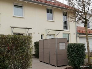 . Reihenhaus mit kleinem Gartenhaus, Hecken und Baum im Vordergrund.